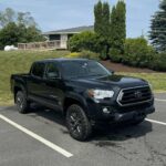 Side view of a black Toyota Tacoma SR5 pickup truck parked in a lot on a sunny day, showing the driver's side with black wheels and extended cab.