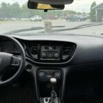 Interior view of a Dodge Dart vehicle showing the dashboard, steering wheel, center console, and front windshield with a road and trees visible outside.